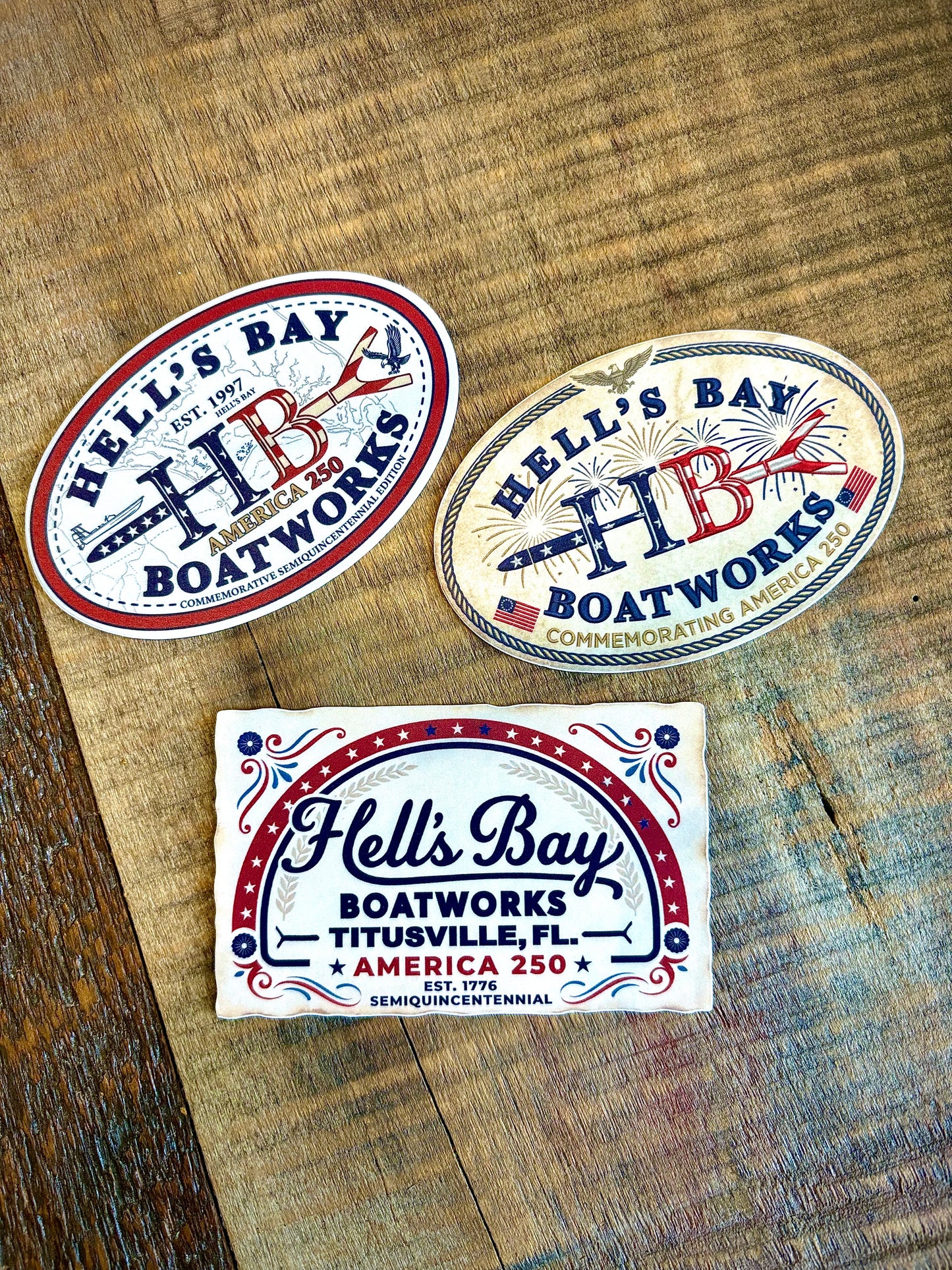 
                  
                    Hell’s Bay Boatworks America 250 sticker pack with three patriotic commemorative decals on a wood tabletop
                  
                