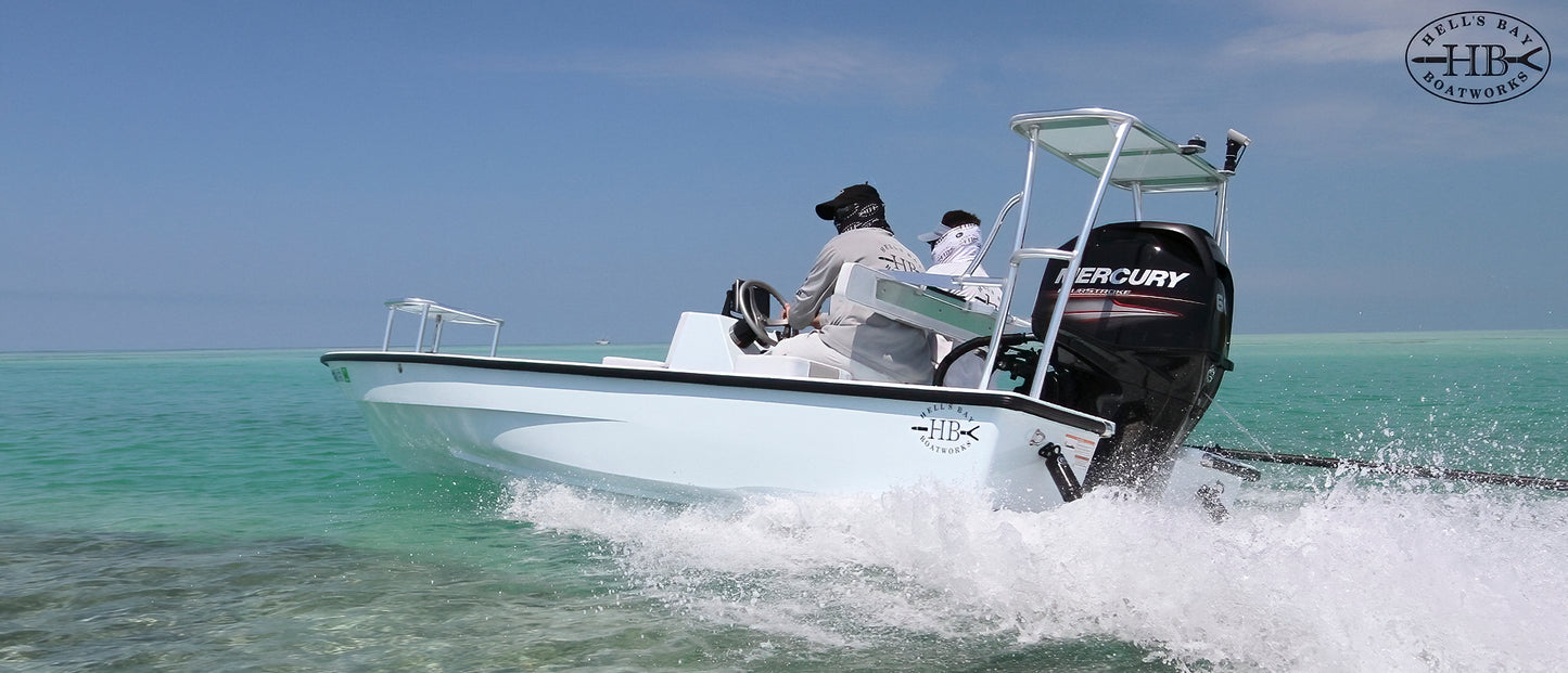 Hell’s Bay Boatworks skiff running across clear shallow water with a Mercury outboard and two anglers aboard.